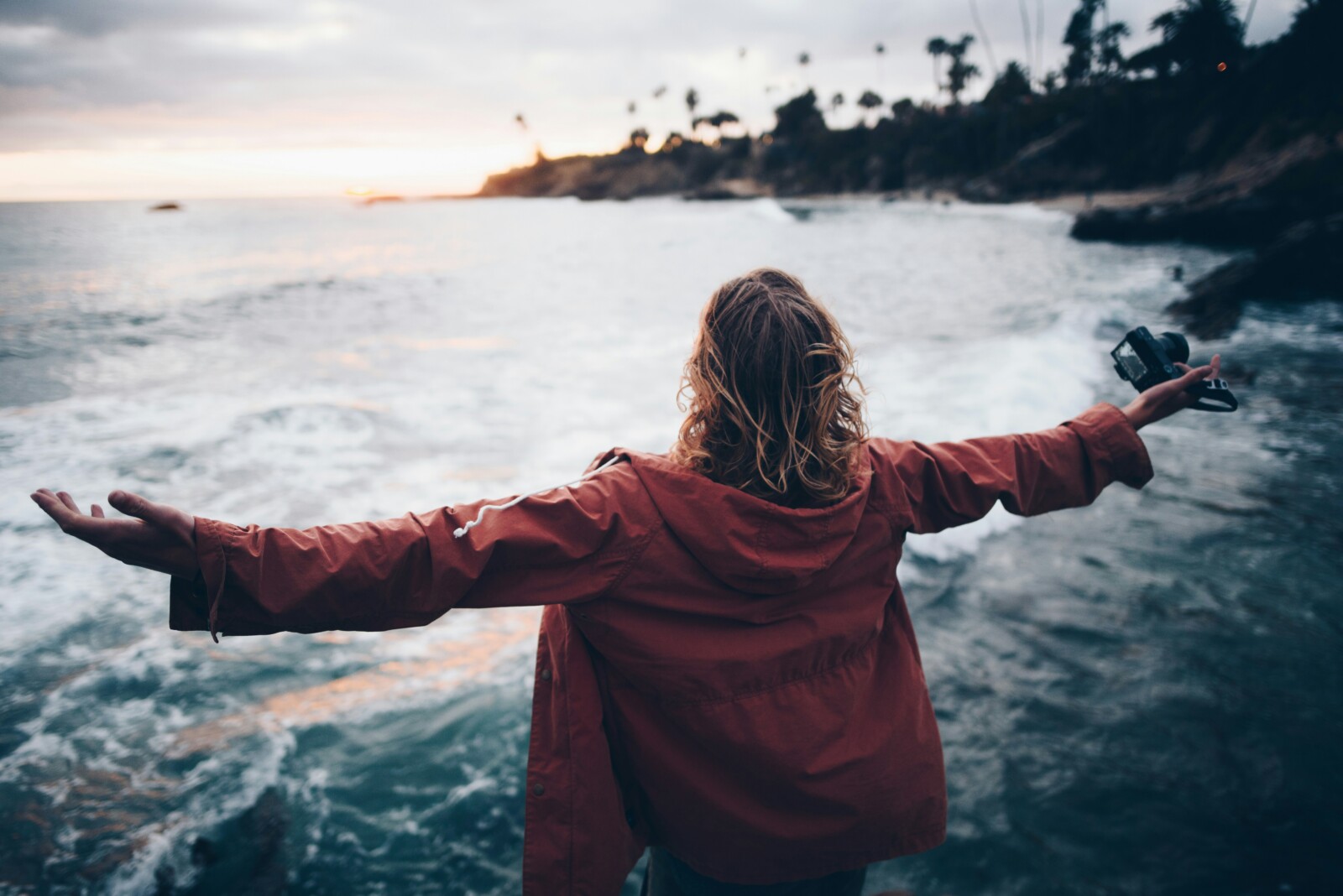 World for the taking: Woman standing by a beach with her arms out as the wind blows her wet hair watching the sunset.
