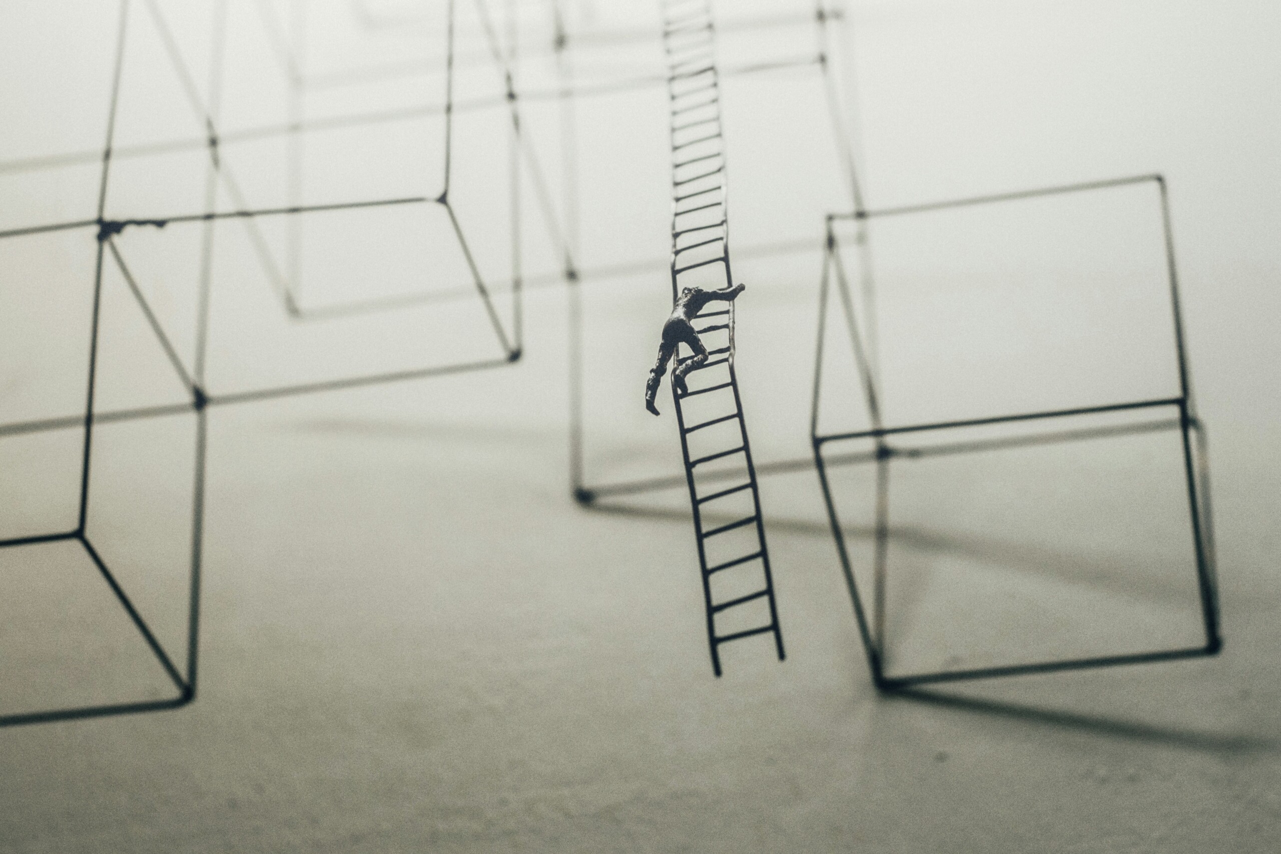 Small figure of a person trying to hang on and climb on precariously to a swinging ladder.