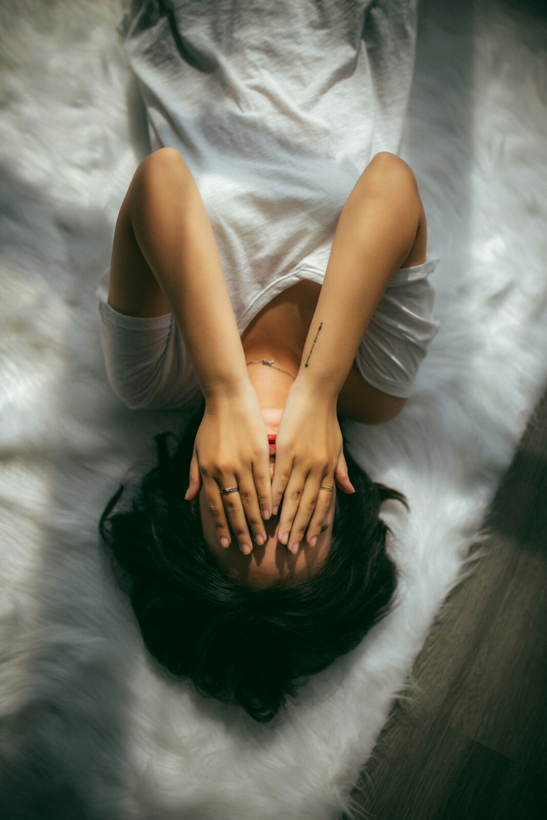 Person lying awake in bed, stressed and overwhelmed with hands covering her face.