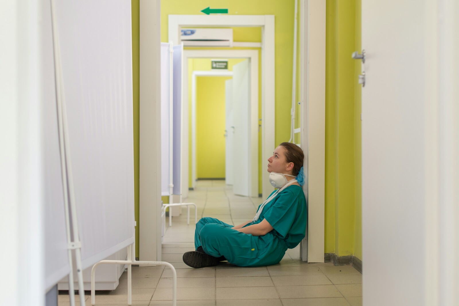 Doctor in scrubs sitting on hospital floor resting with N95 mask around her neck