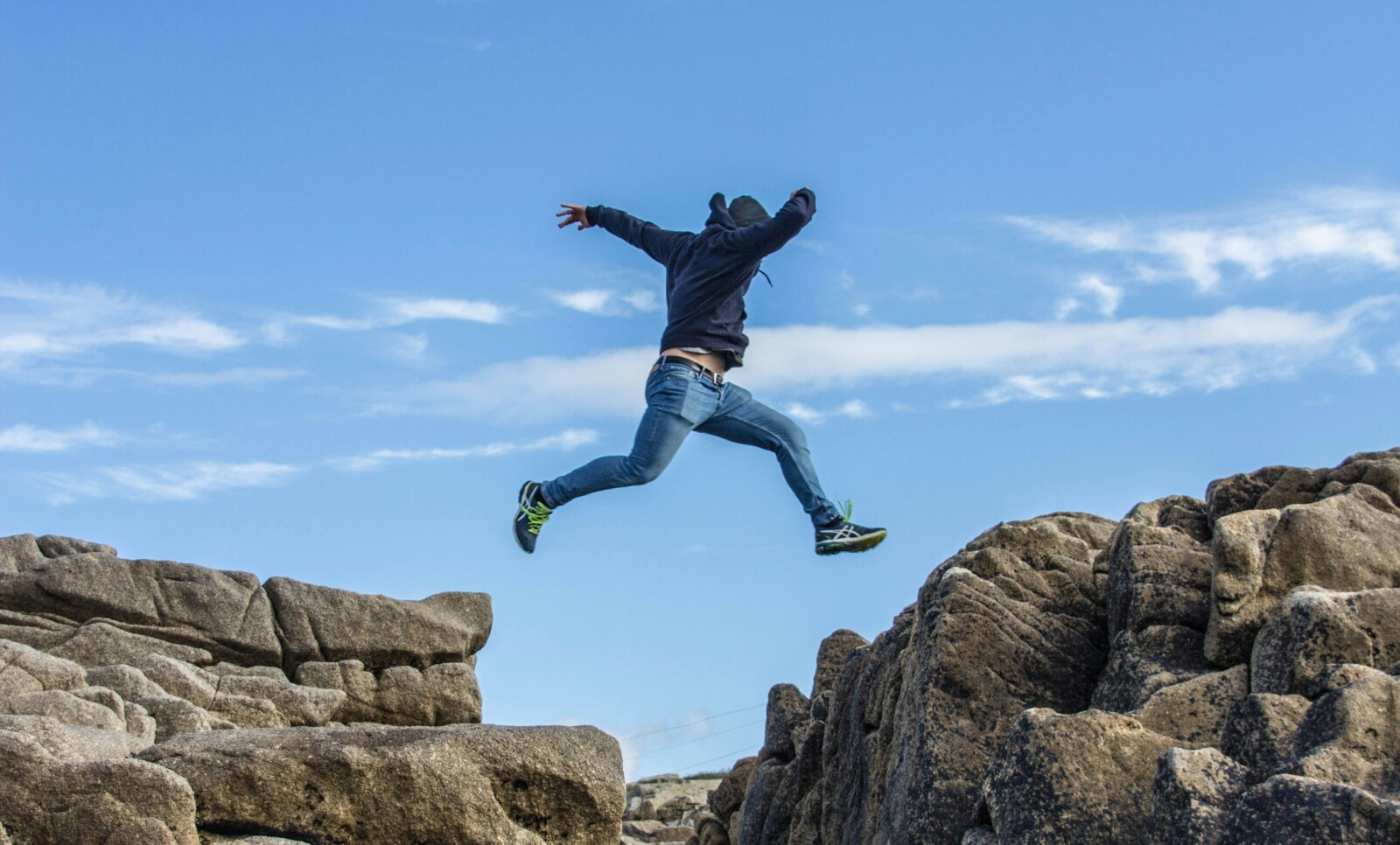 man-in-black-jacket-and-blue-denim-jeans-jumping-on-brown-rocky-mountain-during-daytime