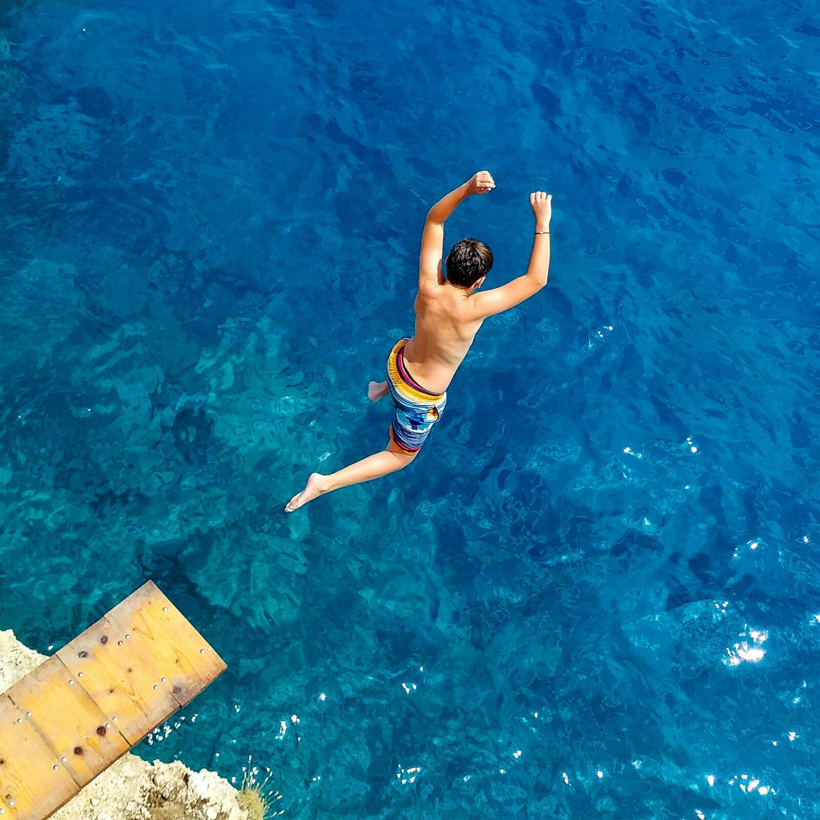 Man jumping into bright blue water during daytime from a diving board