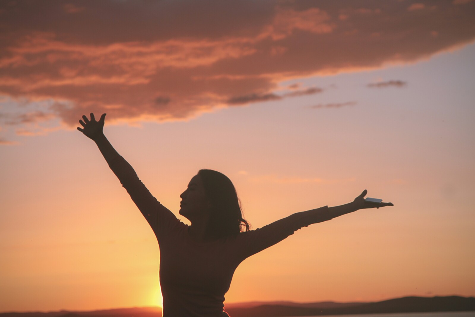 Silhouette of woman in sunset with arms straight out